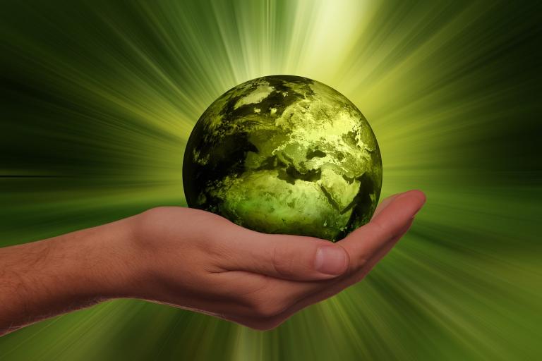 cupping hand holding a green planet with bright rays beaming from the planet.
